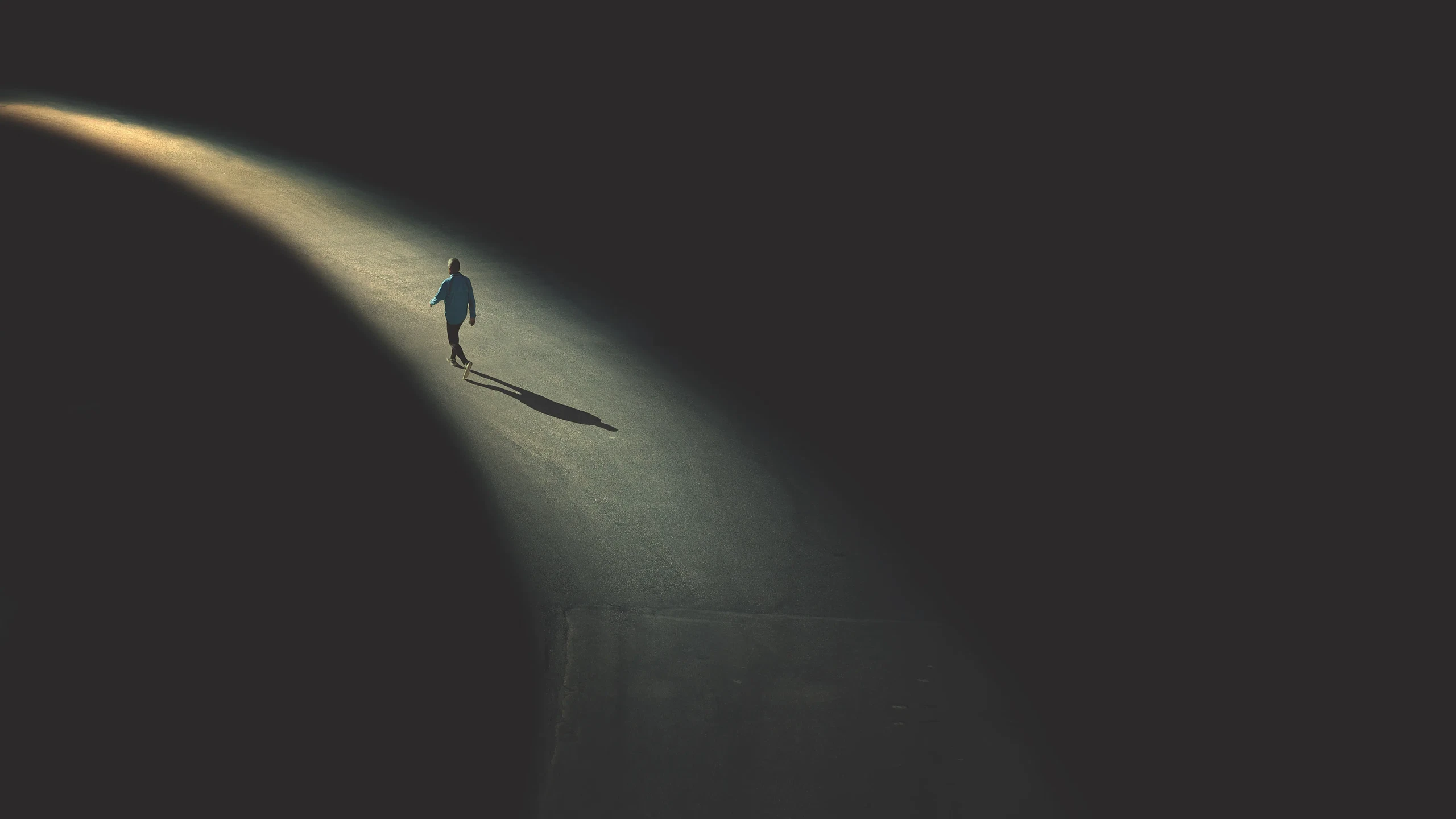  A solitary figure walks down a dimly lit road, creating a long shadow under the contrasting light source. 