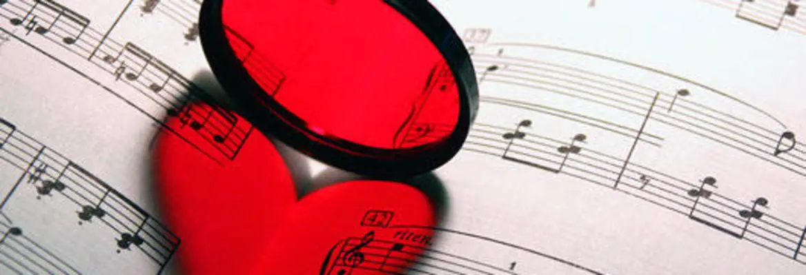 A red heart shape is placed on sheet music, with a black filter creating a striking visual contrast against the musical notes.