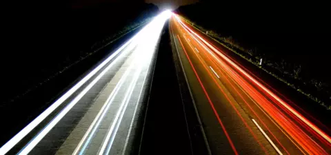 Long-exposure nighttime photograph of a highway, showcasing streaks of white and red lights from vehicles traveling in opposite directions.