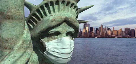 The Statue of Liberty wearing a face mask, set against the skyline of New York City.