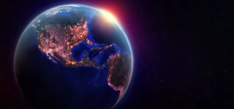 A view of Earth from space, showcasing North and South America illuminated by city lights under the curvature of the planet against a starry backdrop.