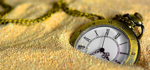 A vintage pocket watch partially buried in fine sand, symbolizing the passage of time and nostalgia.