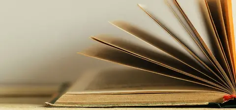 An open book with pages fanned out, resting on a wooden surface against a neutral background.