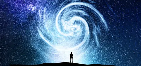 A silhouetted figure stands on a hilltop, gazing up at a mesmerizing spiral of stars and cosmic light in a dark, expansive sky.