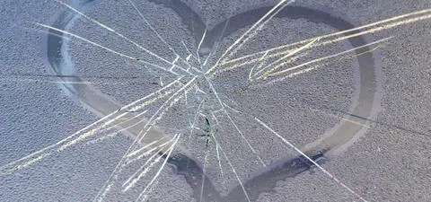 A cracked, frosted surface with a heart shape outlined in moisture; the cracks radiate from the center, creating a striking contrast.