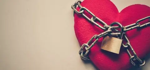 A plush red heart wrapped in metal chains and locked with a padlock, symbolizing concepts of love, security, and protection.