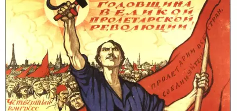 A historic propaganda poster celebrating the Fifth Anniversary of the Great Proletarian Revolution, featuring a worker holding a hammer and sickle against a backdrop of a rallying crowd and Red flags.