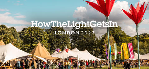 Festival scene in London featuring large, colorful flower sculptures, tents, and vibrant decorations, set against a backdrop of trees and clouds.