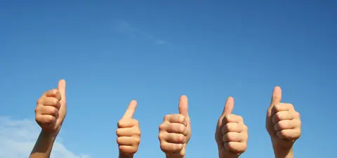 A group of hands with thumbs up against a clear blue sky, symbolizing positivity and approval.