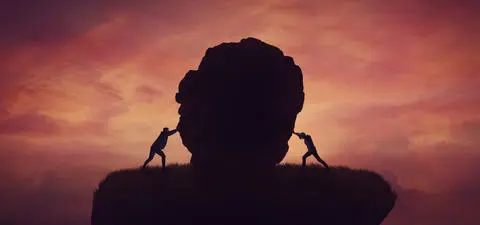 Two figures push against a large rock silhouette against a dramatic sunset sky, symbolizing struggle and perseverance.