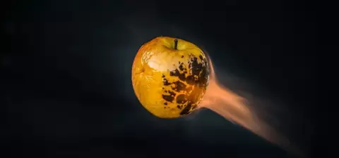 A floating, scorched yellow apple with a trail of flame against a dark background.
