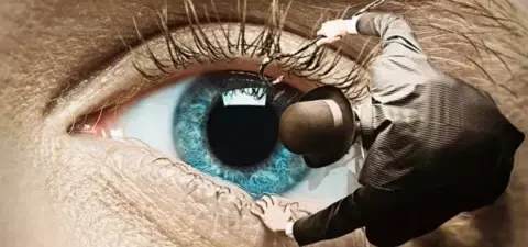 A close-up of a large human eye with a tiny figure in a suit and top hat delicately manipulating the eyelid as if performing an act of precision work.