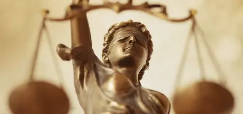 A close-up of a bronze statue of Lady Justice, featuring a blindfolded woman holding a set of scales, symbolizing fairness and impartiality in the law.