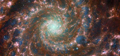 A vibrant, colorful depiction of a spiral galaxy, showcasing swirling patterns of stars, dust, and glowing gas against a darker cosmic background.