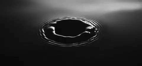 A close-up of a circular ripple in dark water, highlighting the motion and texture created by a disturbance.