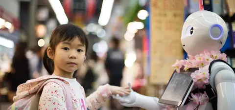 A young girl in a pink backpack interacts with a humanoid robot adorned with flowers, set in a bustling market environment.