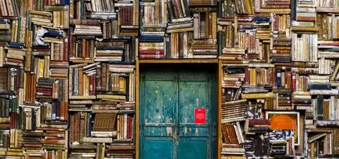 A door surrounded by an eclectic arrangement of stacked vintage books forming a colorful wall, creating a surreal and artistic atmosphere.
