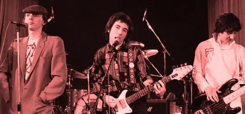 A retro-styled image of a three-member band performing on stage, with a microphone, electric guitar, and bass guitar. The background features drums and instruments.