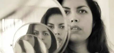 A young woman gazes thoughtfully into a round mirror, reflecting her image and adding depth to the composition.