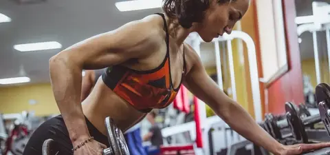A woman performs a bent-over dumbbell row in a gym, concentrating on her workout, showcasing strength and focus.