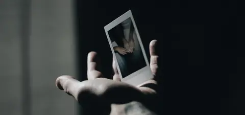 A hand holds a small polaroid photo depicting two hands clasped together, set against a dark background.