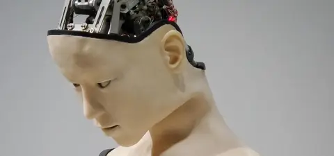 A humanoid robot with a partially exposed mechanical head, showing intricate internal wiring and components, while the facial expression is neutral and contemplative.