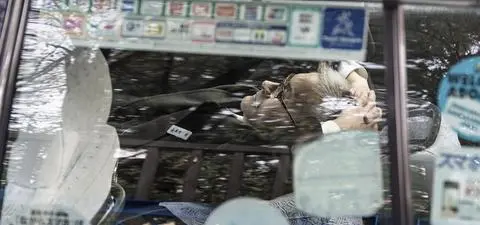 A person with glasses is seen resting inside a taxi, with reflections of city surroundings visible on the glass.