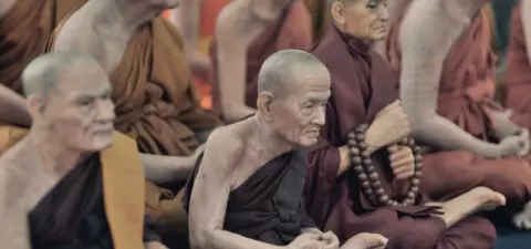 A group of life-like statues representing Buddhist monks, seated in meditation attire, displaying serene expressions and traditional props like prayer beads.