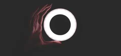 A hand holds a circular, glowing ring against a dark background, creating a striking contrast.