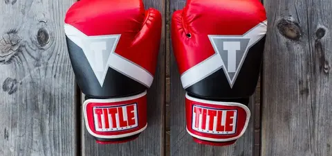 A pair of red and black boxing gloves resting on a wooden surface, featuring the 