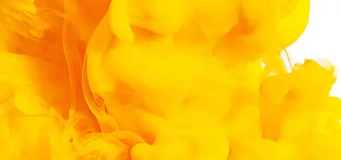 Bright yellow ink or paint swirling in water, creating a dynamic and abstract pattern against a white background.