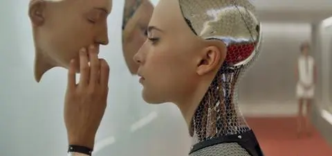 A humanoid robot with a metallic surface examines a removable mask while a woman in the background observes, highlighting themes of identity and artificial intelligence.