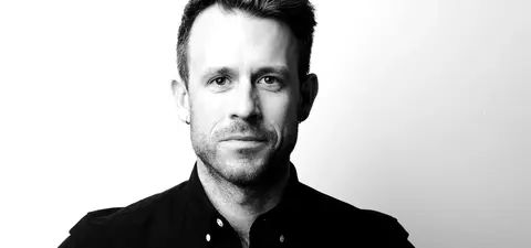 A close-up black and white portrait of a man with short hair, wearing a collared shirt, against a plain background.