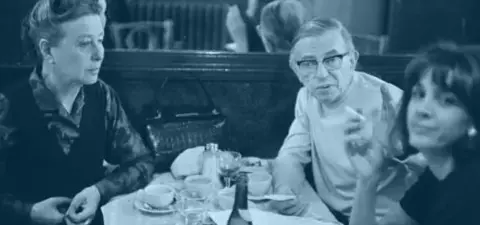 A group of three people seated at a table in a café, engaged in conversation, with cups and plates around them.