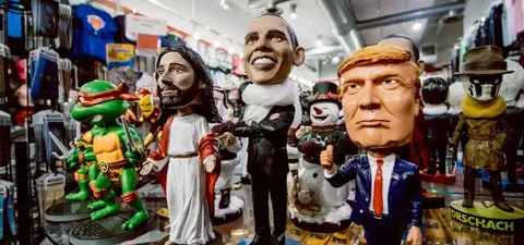 A collection of bobblehead figurines, including Jesus Christ, Barack Obama, Donald Trump, and a turtle character, displayed among various merchandise in a store.