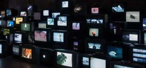 A dark room filled with multiple vintage televisions displaying various images and videos, creating a visually striking and chaotic installation.