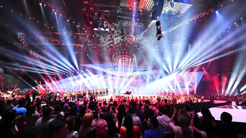 A vibrant stage lit with colorful lights, featuring performers and an enthusiastic audience at a live event, creating an electrifying atmosphere.