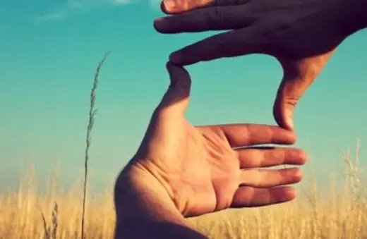 Two hands forming a frame against a blue sky and grassy field, creating a visual focal point in nature.