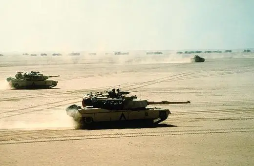 Military tanks maneuvering on a sandy desert landscape, creating dust clouds in the dry environment, with additional tanks visible in the background.