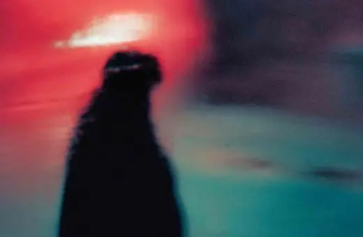 A blurred silhouette of a bottle against a vibrant, abstract background with red and blue hues.