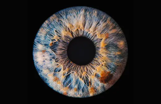 A highly detailed, colorful close-up of a human eye reflecting intricate patterns and hues within the iris, set against a black background.