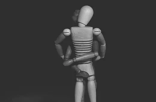 A wooden artist mannequin stands facing away, hands on hips, set against a dark background, showcasing its articulated joints and neutral pose.