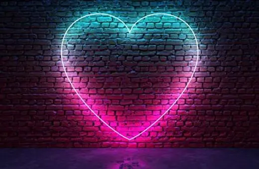 A glowing neon heart outline in vibrant pink and blue against a textured brick wall.