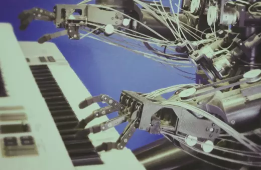 A robotic hand interacting with a keyboard, showcasing intricate mechanics and wiring, set against a blue background.