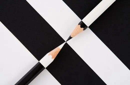 Two pencils, one black and one white, intersect at the center of a black and white checkerboard pattern.