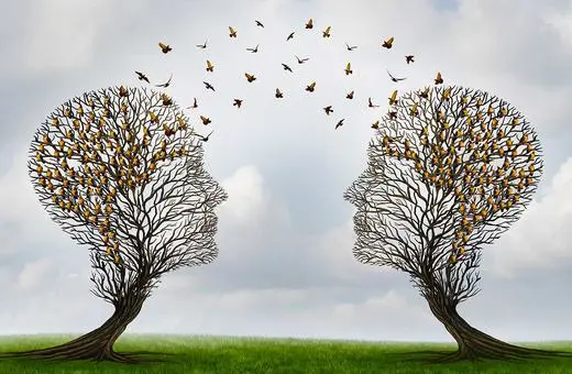 Two tree silhouettes shaped like human heads face each other, with butterflies flying around them against a cloudy sky.