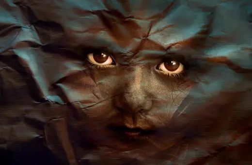 A close-up of a child's face partially obscured by textured, crumpled layers, creating a mysterious and surreal effect with deep, expressive eyes.