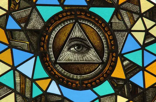 Stained glass window featuring a prominent Eye of Providence within a triangle, surrounded by colorful geometric shapes.