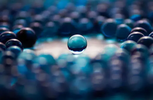 A single clear marble surrounded by a ring of blue marbles, creating a striking visual contrast.