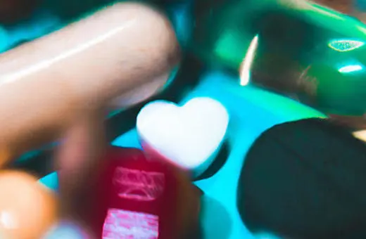 A collection of various pills and capsules in different shapes and colors, including a white heart-shaped pill and a black round pill.